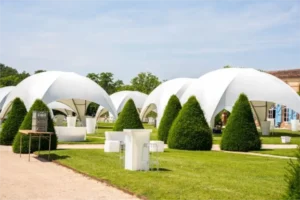 Dômes blancs dressés sur la pelouse d’un château, entre les ifs taillés, pour une garden party d’entreprise