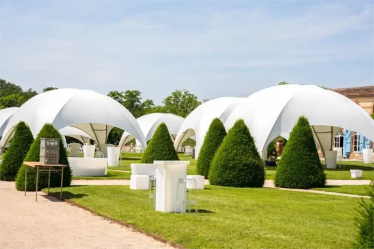 Dômes blancs dressés sur la pelouse d’un château, entre les ifs taillés, pour une garden party d’entreprise