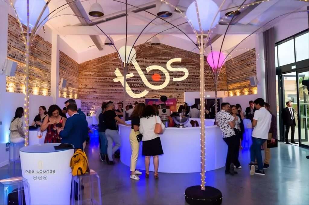 Diplômés et familles réunis autour d’un bar lumineux sous des luminaires en ombrelle, réception après une remise de diplômes à Toulouse
