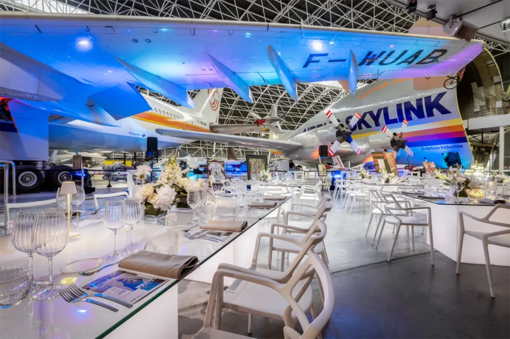 Dîner de gala dressé sous les avions du musée Aeroscopia, tables blanches et éclairage bleu