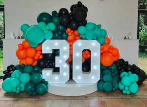 Chiffre 30 lumineux entouré d'une arche de ballons verts, orange et noirs