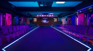 Défilé événementiel avec podium central éclairé en violet et bleu, ambiance immersive avec éclairages LED et scène au fond.