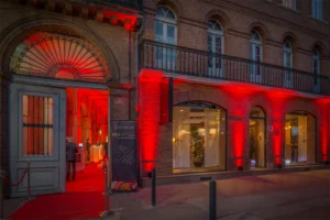 Façade d'un hôtel particulier illuminée en rouge, tapis rouge à l'entrée