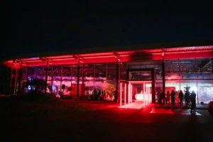 Bâtiment vitré éclairé en rouge, invités rassemblés à l'extérieur de nuit