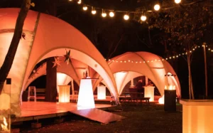 Chapiteaux éclairés en orange sous les arbres, guirlandes guinguette
