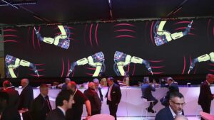 space événementiel aménagé par PSB Lounge à Toulouse : mobilier lounge, bar et mange-deboudevant un écran LED géant diffusant une animation de bras robotisés lors d’un événement industriel.