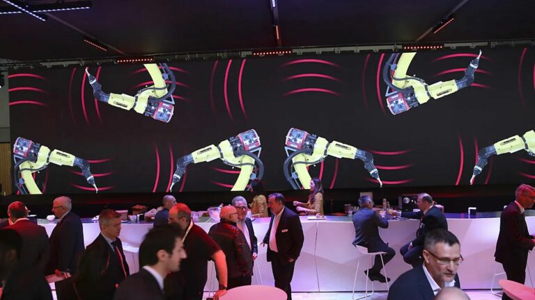 space événementiel aménagé par PSB Lounge à Toulouse : mobilier lounge, bar et mange-deboudevant un écran LED géant diffusant une animation de bras robotisés lors d’un événement industriel.