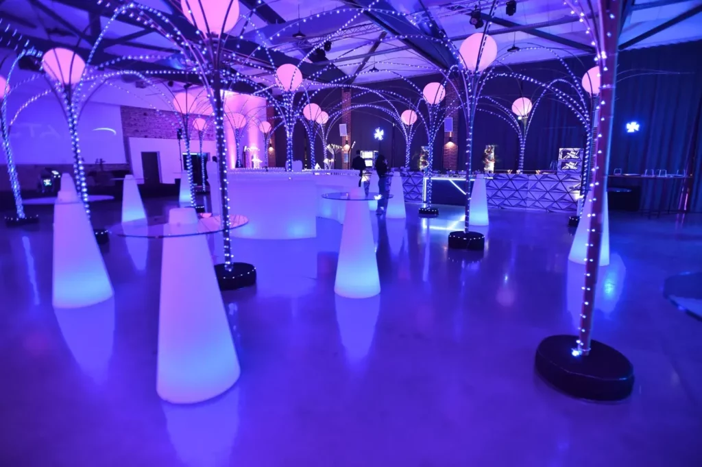 Mange-debout lumineux , bar centrale et structures décoratives éclairées en bleu et violet dans une salle événementielle.