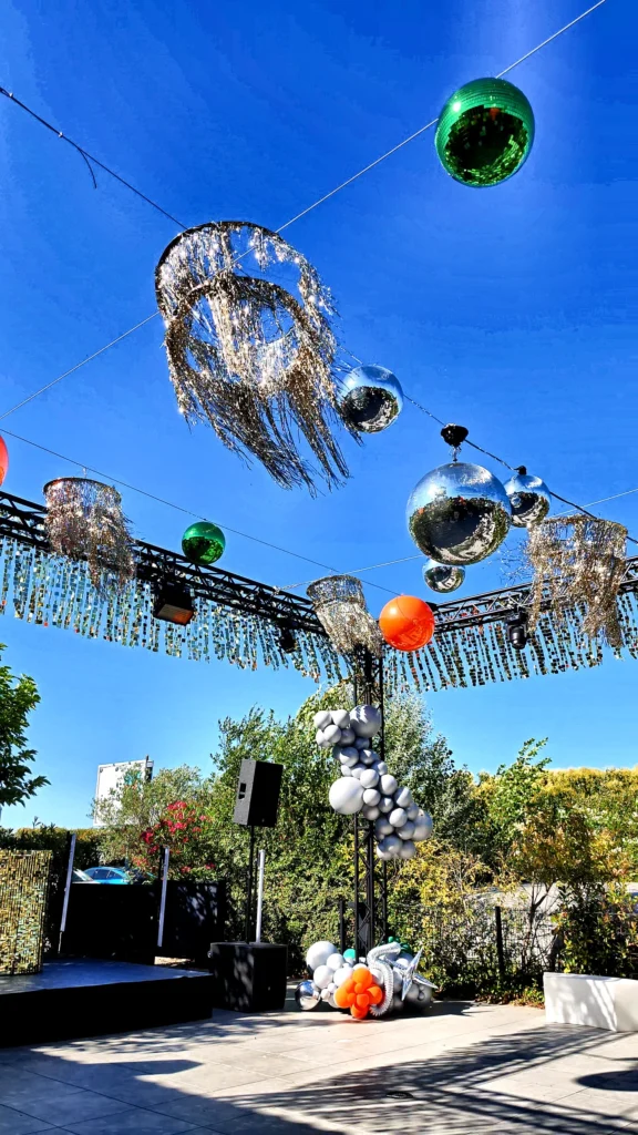 Contre-plongée sous la structure habillée en plein soleil, lustres à franges et sphères suspendues — Manoir du Prince, soirée d'entreprise en Occitanie.