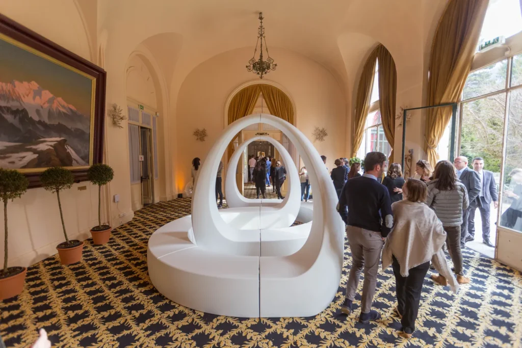 Invités réunis autour d'un banc Boucle AND blanc, dans un salon aux tentures dorées