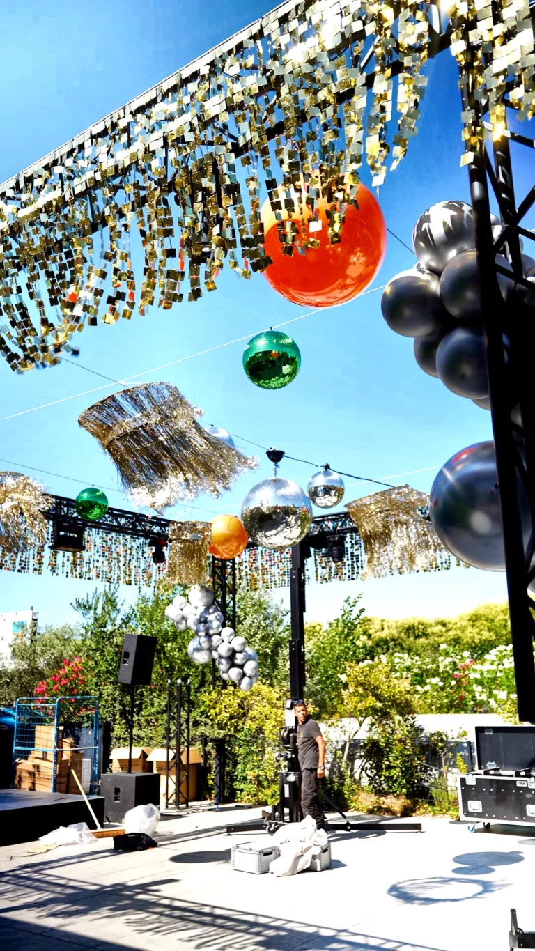 Contre-plongée sur la terrasse habillée en plein soleil, sequins, sphères et ballons — scénographie lumineuse PSB Lounge.