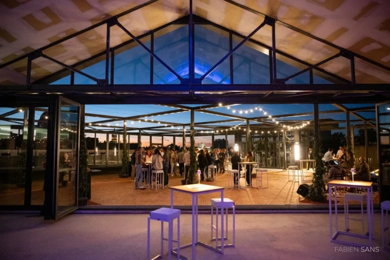 Toit-terrasse des Variétés à Toulouse à l’heure bleue, vu depuis la halle : guirlandes à ampoules, mange-debout et invités sous l’ossature métallique